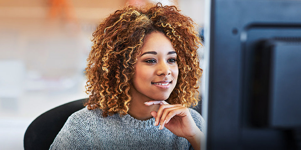 The image shows a woman smiling at her computer screen as she discovers the benefits of an Automated Email processing and classification system that leverages powerful AI-driven intelligent document processing (IDP) technology.