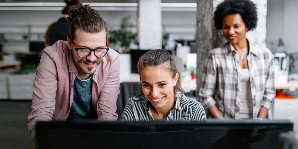 The image shows three employees in front of a computer learning about the benefits of software automation solutions automate workflows and improve employee satisfaction.