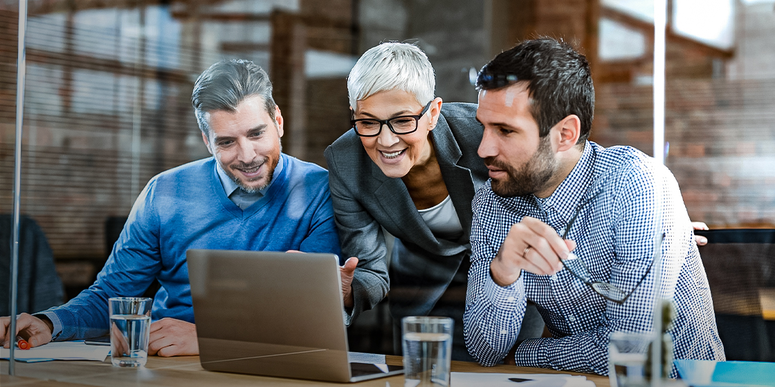 the image represents a group of people collaborating and using technology to work more efficiently and effectively. The laptop and the Automation Hero software running on it automate various tasks, allowing the group to focus on more complex and creative work. While artificial intelligence can perform many tasks that were previously done by humans. The people in the image are using technology to work together and achieve their goals, highlighting the importance of both software automation and artificial intelligence in modern work environments.
